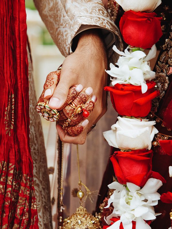 Authentic indian bride and groom's hands holding together in traditional wedding attire and red and white roses